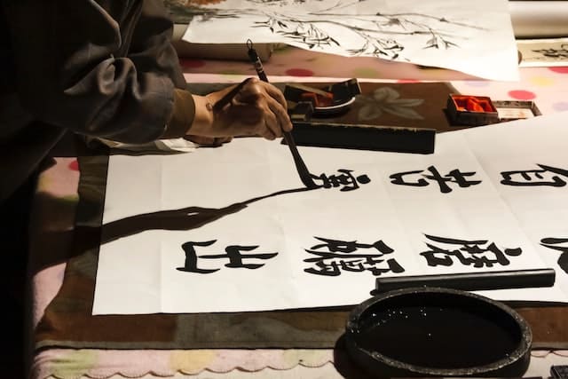 alguien escribiendo en estilo kaisho kanjis don tinta china sobre papel de arroz