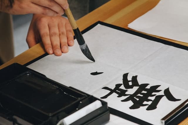 Alguien está usando un pincel de bambú. Escribe sobre papel de arroz un kanji.
